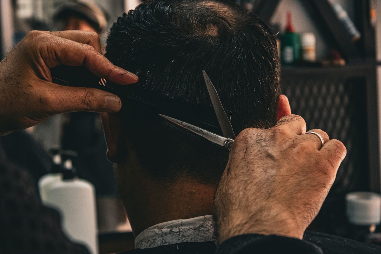 about-img Close-up of a barber expertly cutting a client's hair, highlighting traditional grooming skills.
